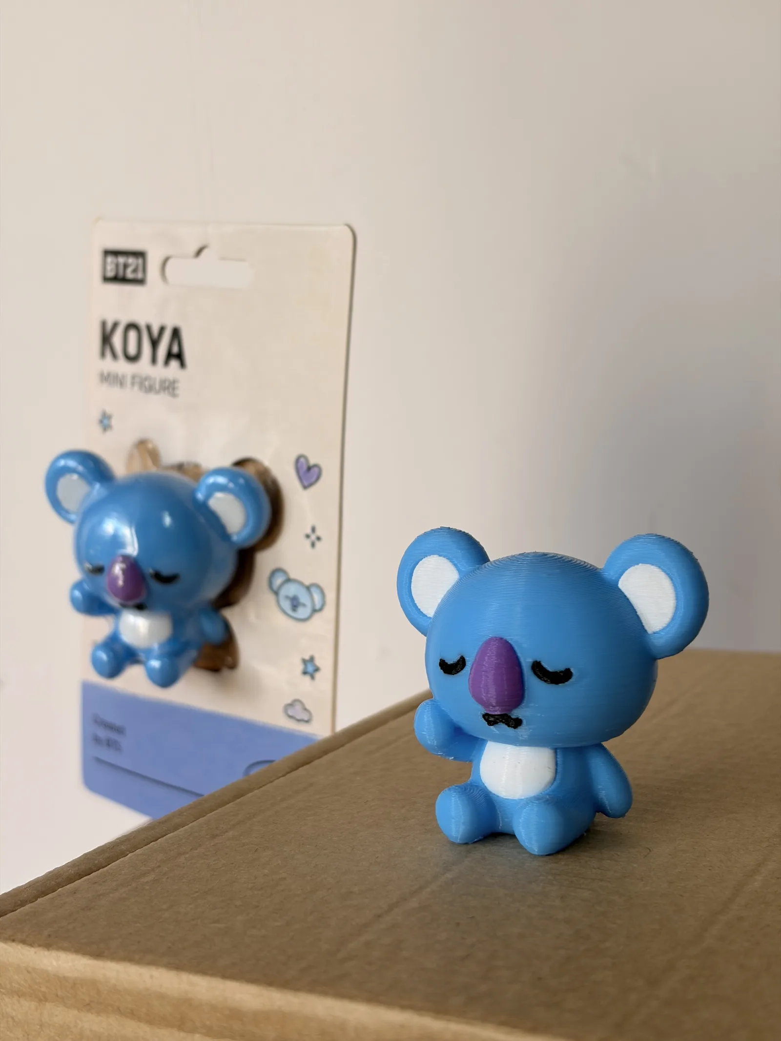Mini figura de Koya impresa en 3D junto a su blíster