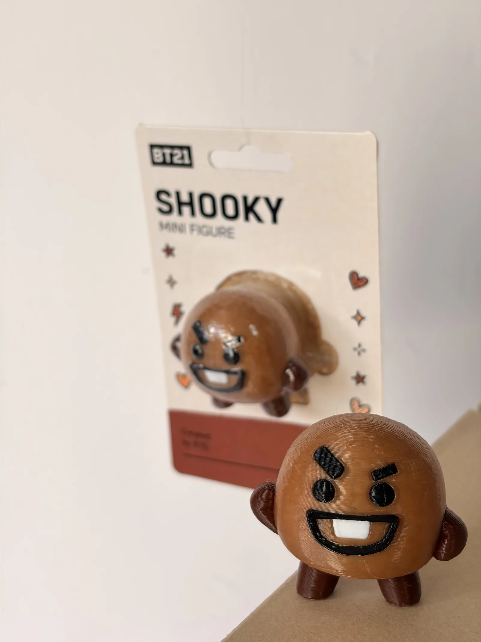 Mini figura de Shooky impresa en 3D junto a su blíster